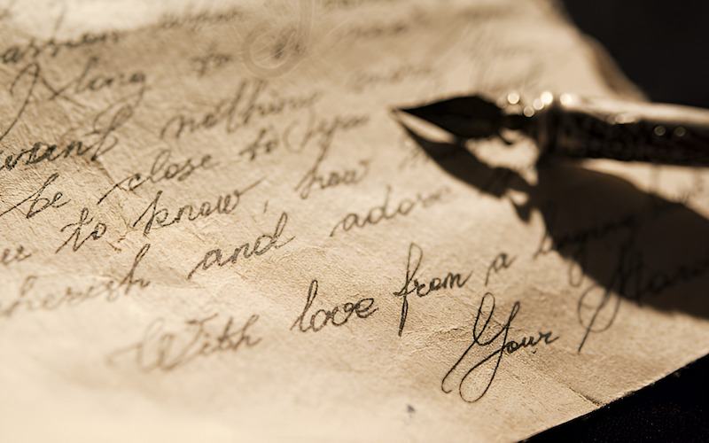 Một người đang viết thư tay trên bàn gỗ với hoa trang trí.