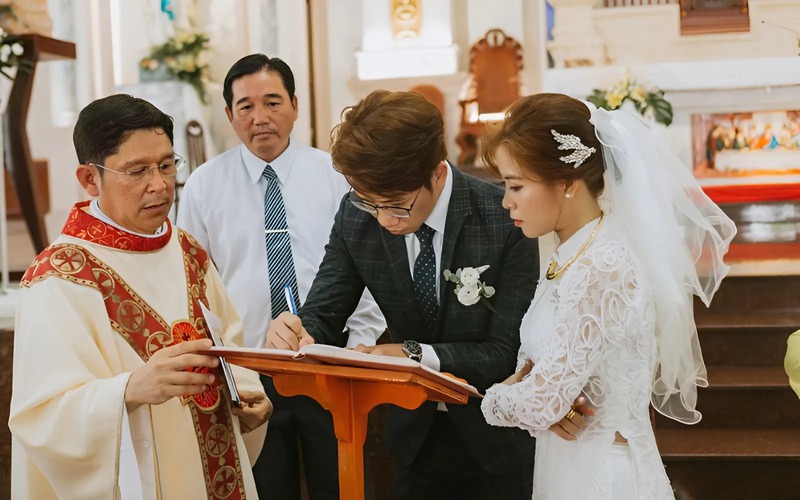 Cặp đôi cùng nhau ký tên vào sổ hôn phối với sự chứng kiến của linh mục
